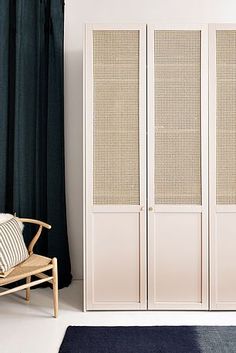 a room with a blue chair and white cabinet next to a black curtained window