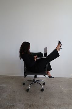 a woman sitting in an office chair with her feet up on the desk while using a laptop computer