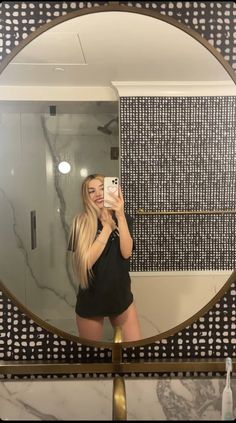 a woman taking a selfie in front of a bathroom mirror with her cell phone