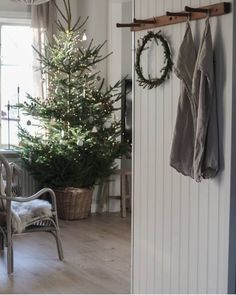 a christmas tree in the corner of a room with a coat rack and chair next to it