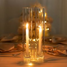 two tall clear vases with lit candles on a table