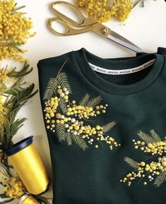 a green sweater with yellow flowers on it next to a pair of scissors and some plants