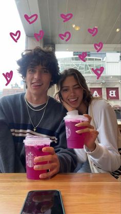 two people sitting at a table with drinks in front of them and hearts flying above