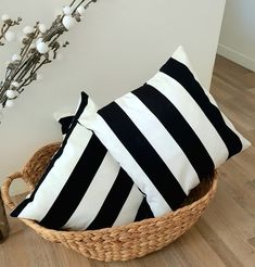 two black and white pillows in a basket next to a vase with flowers on it