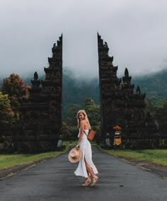 a woman in a white dress is walking down the road with a hat on her head