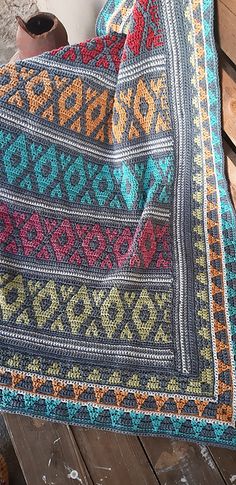 a colorful blanket sitting on top of a wooden bench next to a vase and cup