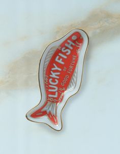 a red and white fish shaped pin with the words lucky fish on it's side