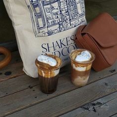 two cups of coffee sitting on top of a wooden table next to a brown bag