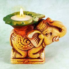 an elephant figurine with a lit candle in it's trunk on a white background