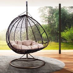 a hanging egg chair on a wooden floor in front of a large window with trees