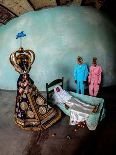 two men in blue suits stand next to a bed with a woman laying on it