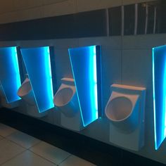 a row of urinals mounted to the side of a wall with blue lights