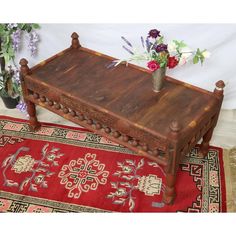 a wooden bench with flowers on top of it in front of a rug and wall