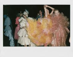 several women in dresses are dancing with feathers on their arms and legs, while one woman is holding her leg up