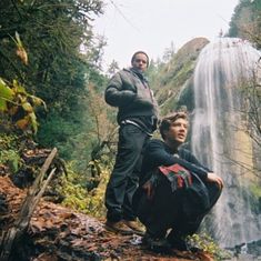 two men standing in front of a waterfall