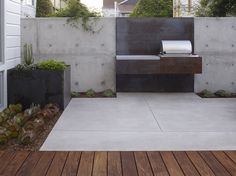 an outdoor kitchen and grill area in a backyard with wood flooring, concrete walls and planters