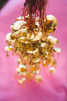 a bunch of gold beads hanging from a pink cloth with water droplets on them and red stems in the background