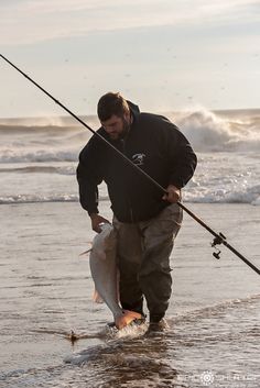 a man standing in the water holding a fish and fishing rod with his right hand