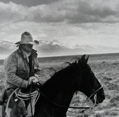 a man riding on the back of a brown horse in an open field with mountains in the background