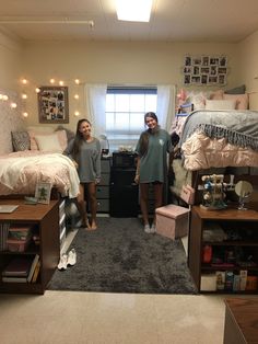 two girls standing in a dorm room with lights on the ceiling and carpeted floor