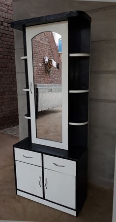 a black and white cabinet with a mirror on it's front door, next to a brick wall