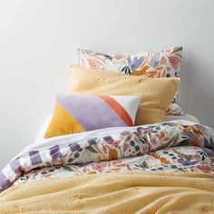 a bed with colorful pillows and blankets on it's headboard, next to a white wall