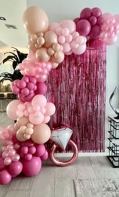 a bunch of balloons that are on the ground in front of a wall with pink and white streamers