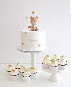 a teddy bear sitting on top of a cake next to cupcakes