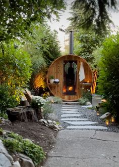 a small wooden cabin in the middle of some trees and bushes with lights on it