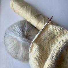 two skeins of yarn next to each other on a white surface with knitting needles