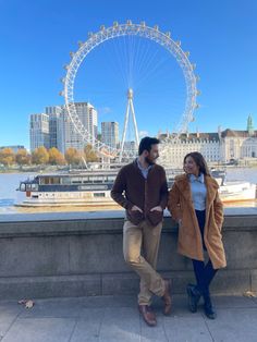 two people standing next to each other in front of a large ferris wheel and buildings