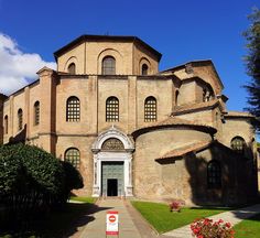 an old building with arched windows on the front and side walls, surrounded by greenery