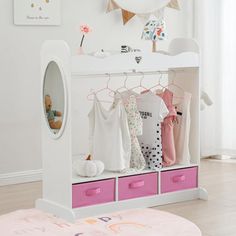 a child's white and pink closet with clothes hanging on the rack, mirror and teddy bear