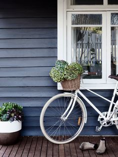 a white bicycle parked in front of a blue house with potted plants next to it