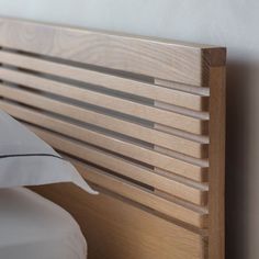 the headboard of a bed with white sheets and wood slats on it's sides