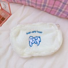 a small white purse sitting on top of a bed next to a pink and blue pillow