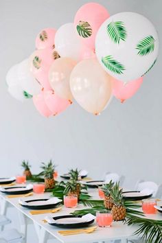 a table topped with lots of balloons and pineapples on top of white plates