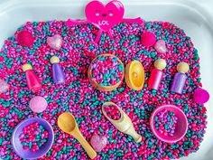 a white tray filled with lots of colorful sprinkles and plastic spoons