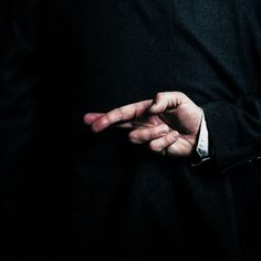 a man in a black suit is holding his hands together