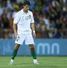 a man standing on top of a soccer field wearing white and green uniform with his hands in his pockets