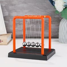 an orange newtons cube with three balls in it on a table next to flowers