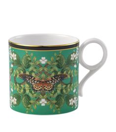 a green and gold coffee cup with a butterfly on the front, surrounded by white flowers