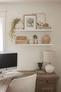 a desk with a computer on top of it next to a lamp and some pictures