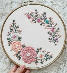 a hand is holding a embroidery hoop with pink and white flowers on it in front of a fluffy rug