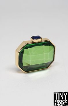 a green and gold ring with a blue stone on the top, in front of a white background