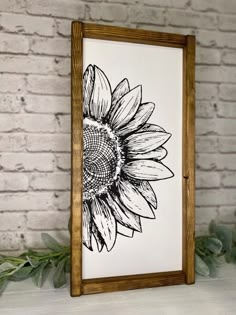 a black and white drawing of a sunflower in a wooden frame on a brick wall