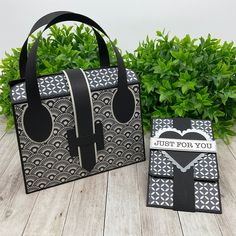 two black and white bags sitting on top of a wooden floor next to green plants