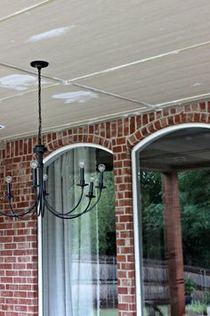 a chandelier hanging from the ceiling in front of a brick wall and patio