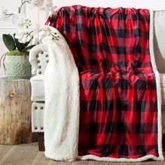 a red and black plaid blanket sitting on top of a chair next to a vase with flowers