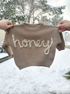 "This listing is for one personalized, hand embroidered baby name / word sweater. These sweaters are the cutest for a baby announcement, baby shower, gender reveal, family photos, 1/2 or 1st birthday and everything in between! They also make the cutest gift! **This listing includes free shipping! I currently offer up to 8 letter names/words on these sweaters. If you would like to do one word or name on top of the other, please say so in the personalization section. Please message me if you are needing more than 8 letters on the sweater. If there is an i in the name, please specify if you would like the dot to be a heart, flower or normal dotted i. These sweaters come in two sizes: 6 month and 12 month. They are made to be chunky and oversized. The 6 month currently comes in all listed colo Cute Winter Sweater With Letter Embroidery, Customizable Cute Winter Sweater, Cute Customizable Winter Sweater, Embroidered Winter Birthday Sweater, Cute Winter Sweater With Embroidered Text, Gender Reveal Family, Honey Sweater, Letter Names, Kid Outfits